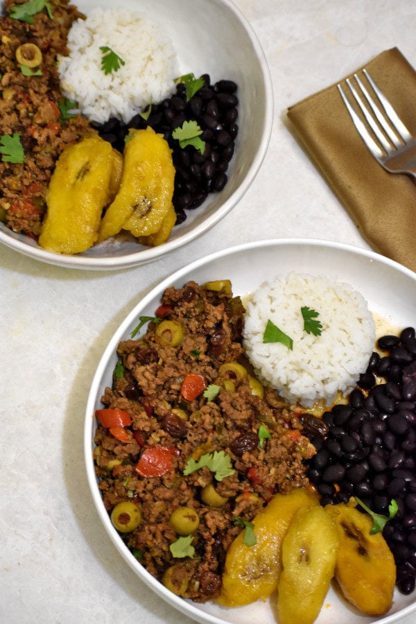 Two bowls of Puerto Rican picadillo with white rice, black beans and plantains.