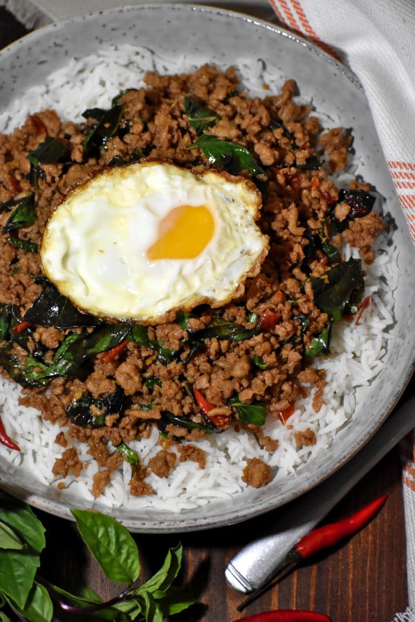 overhead view of thai basil chicken, topped with a fried egg, in a rustic grey bowl