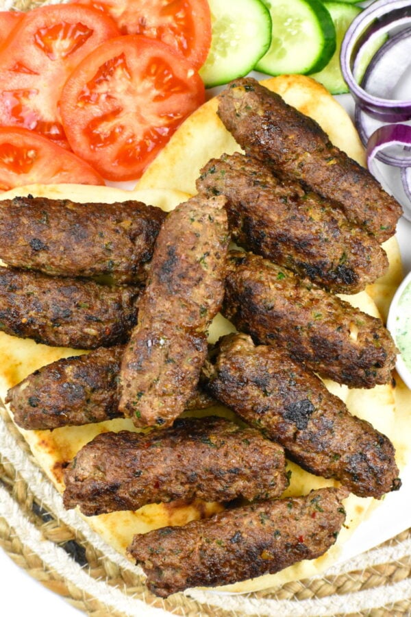 Platter of seekh kebab served with pita and sliced vegetables.