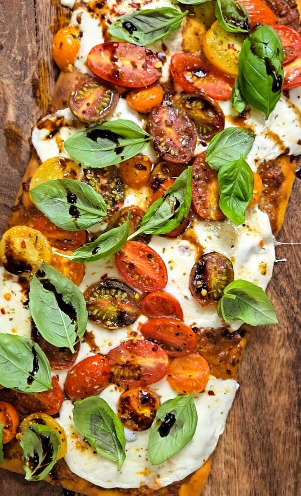 Caprese pesto flatbread on a cutting board.