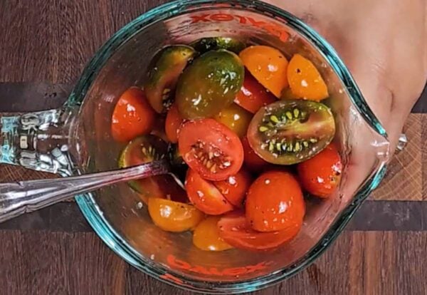 Tossing cherry tomatoes with salt, pepper and olive oil.