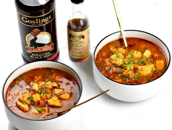 Two bowls of fish chowder along side bottles of rum and sherry.
