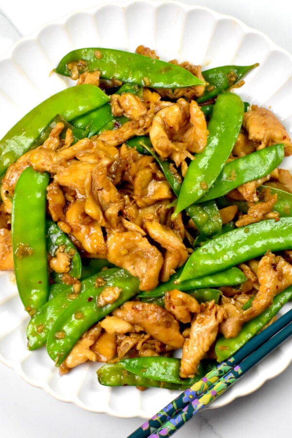 Plat full of chicken and snow peas in a brown sauce.