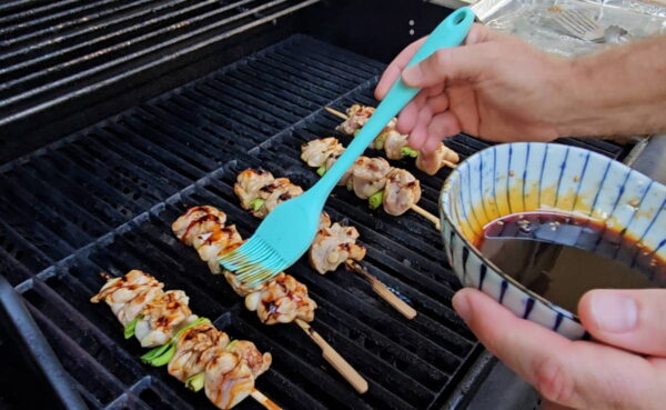 Brushing sauce on the skewers while they grill.